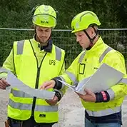 To ansatte i arbeidstøy som ser på dokumenter.