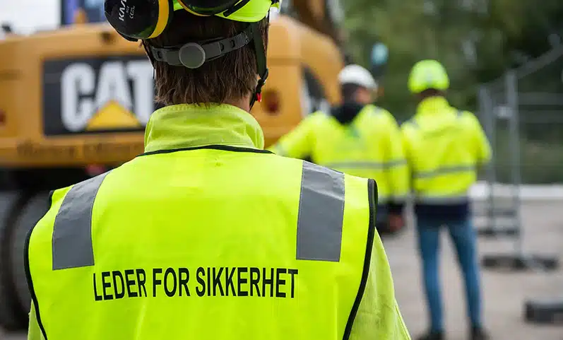 Ansatt som har på seg hjelm og refleksvest der det står "Leder for sikkerhet".